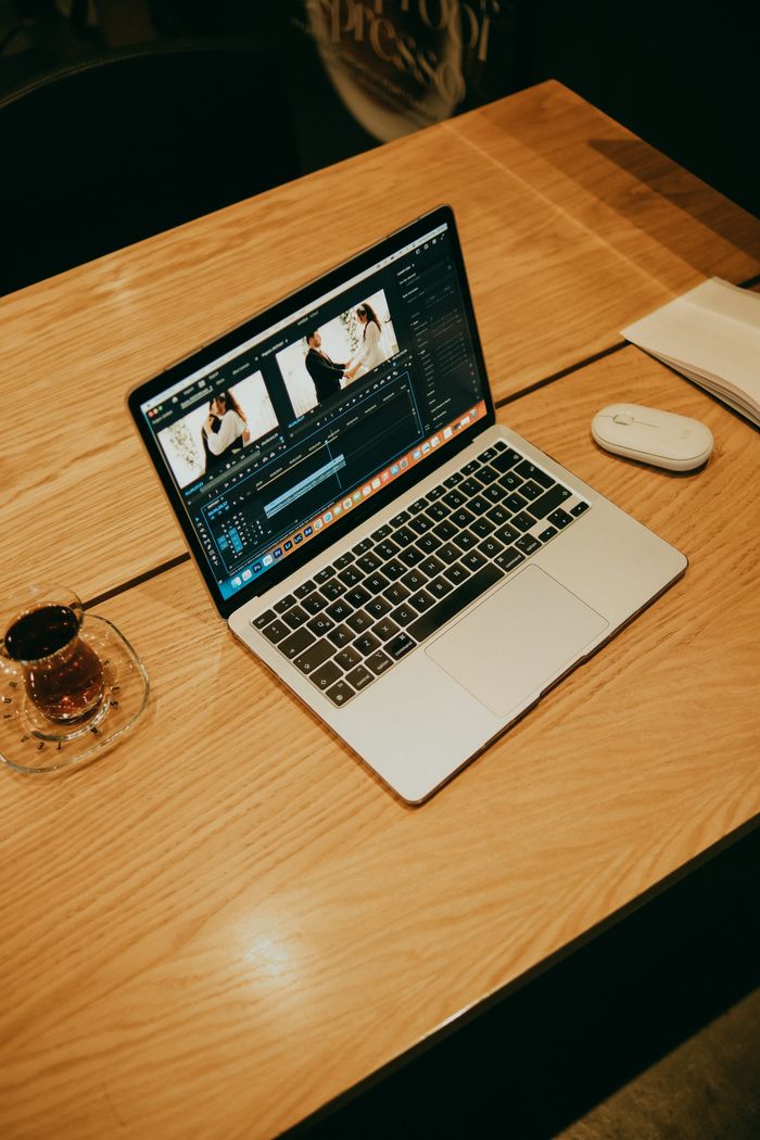 A laptop su un tavolo di legno in un coffee shop, che mostra un software di video editing per un lavoro creativo.